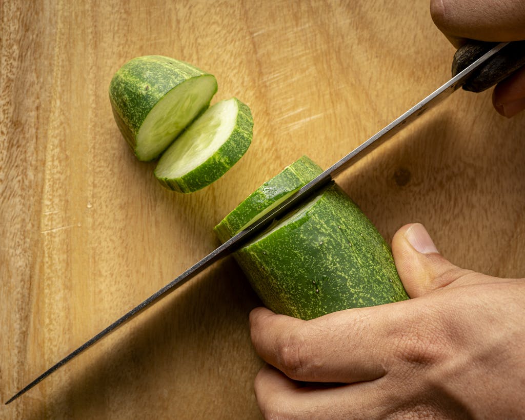 A Person Slicing a Cucumber on Brown Wooden Surface